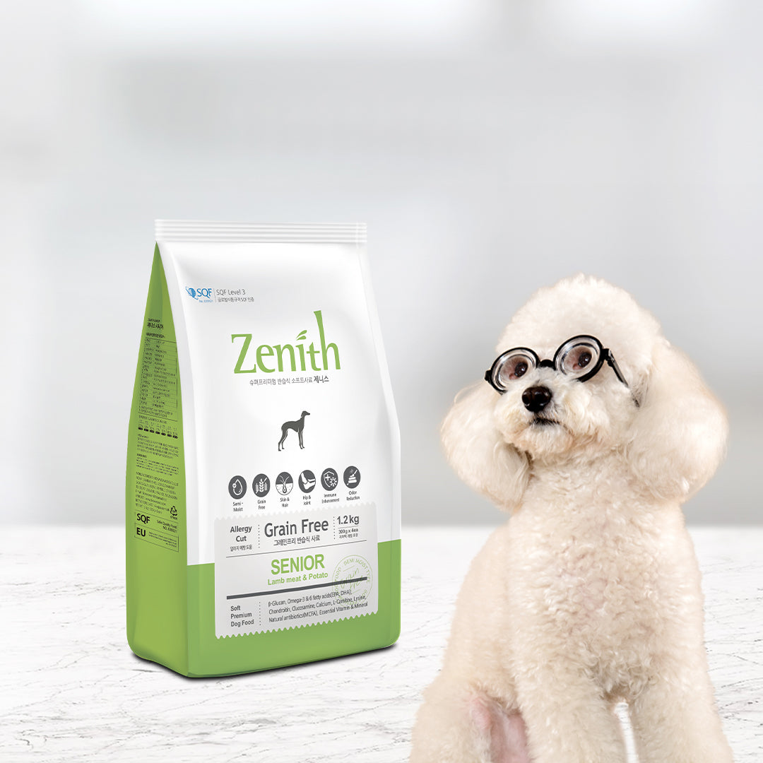 A green bag of Zenith Senior dog food old packaging  stands next to a small cream-colored poodle wearing black glasses, set against a clean, light gray studio background.