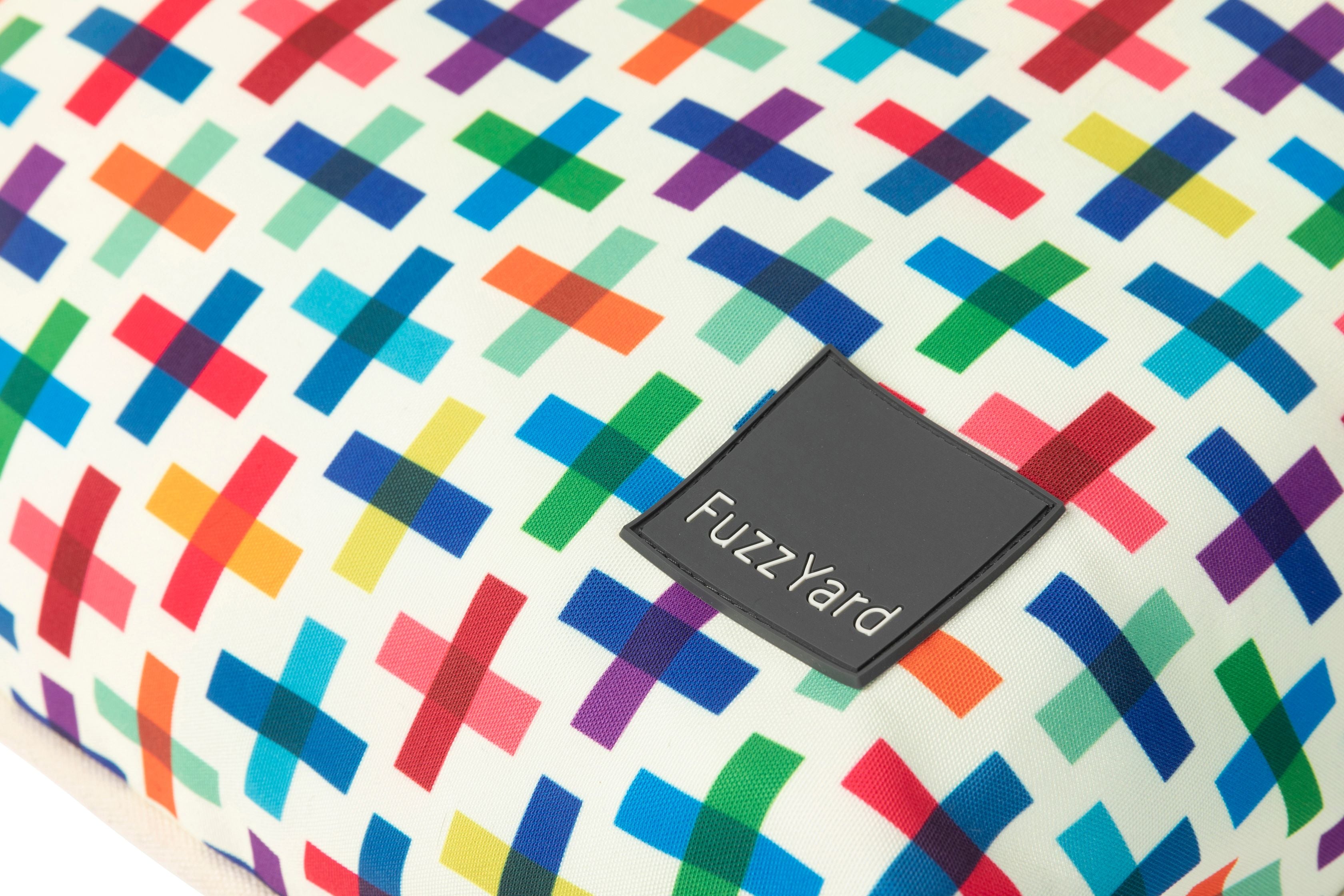 A close-up of a fuzzyard dog bed colorful geometric patterned fabric with a black brand patch reading 'FuzzYard'.