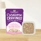 A pouch of Stella & Chewy's Carnivore Cravings grain-free chicken and salmon Recipe wet cat food next to a small white square bowl filled with the actual shredded chicken and salmon meat in broth
