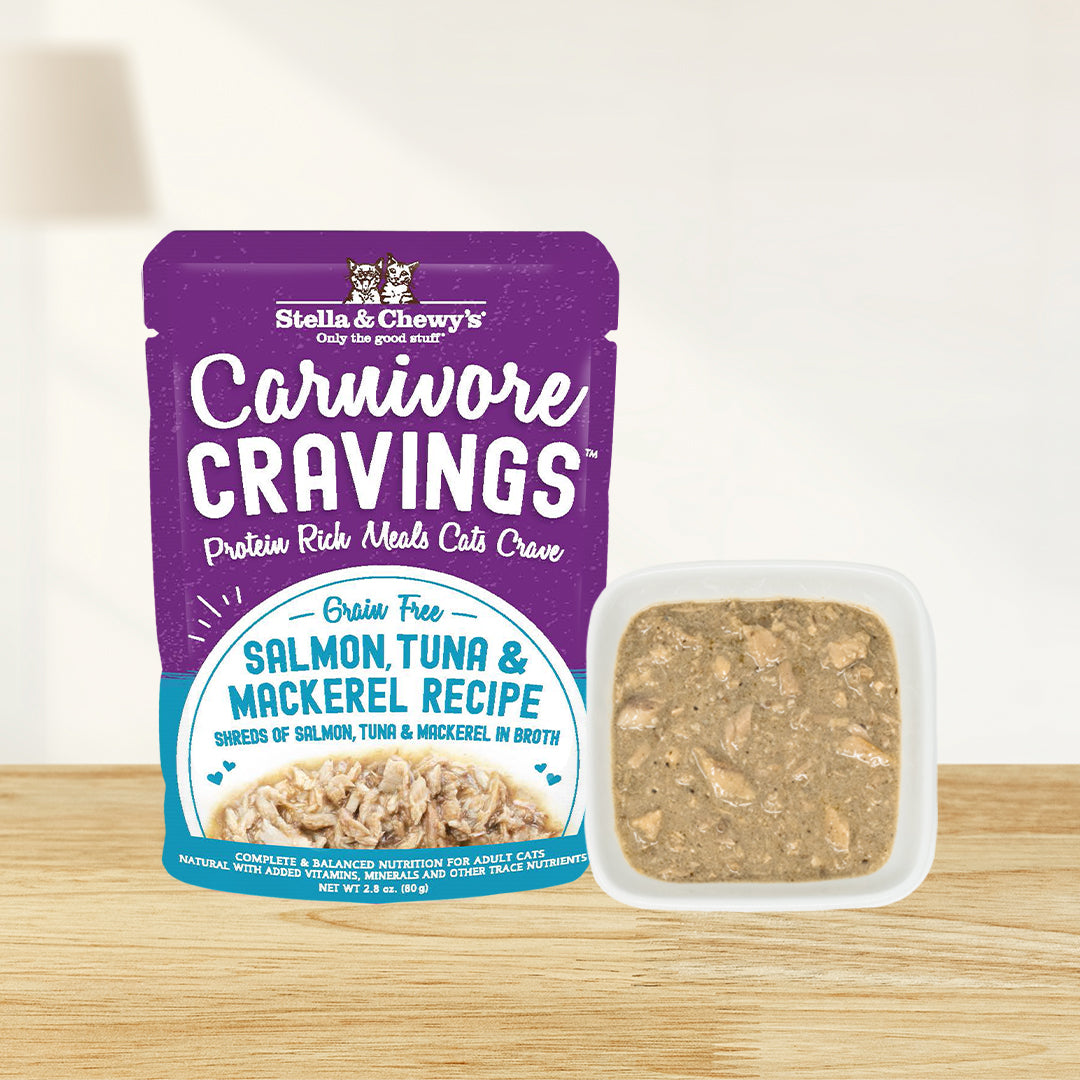 A pouch of Stella & Chewy's Carnivore Cravings grain-free salmon, tuna and mackerel recipe wet cat food next to a small bowl filled with the actual shredded fish meat in broth