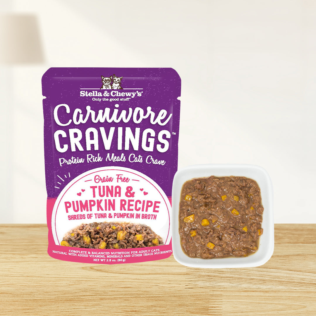A pouch of Stella & Chewy's Carnivore Cravings grain-free Tuna & Pumpkin Recipe wet cat food next to a bowl filled with the actual shredded tuna meat and visible pumpkin chunks in broth.